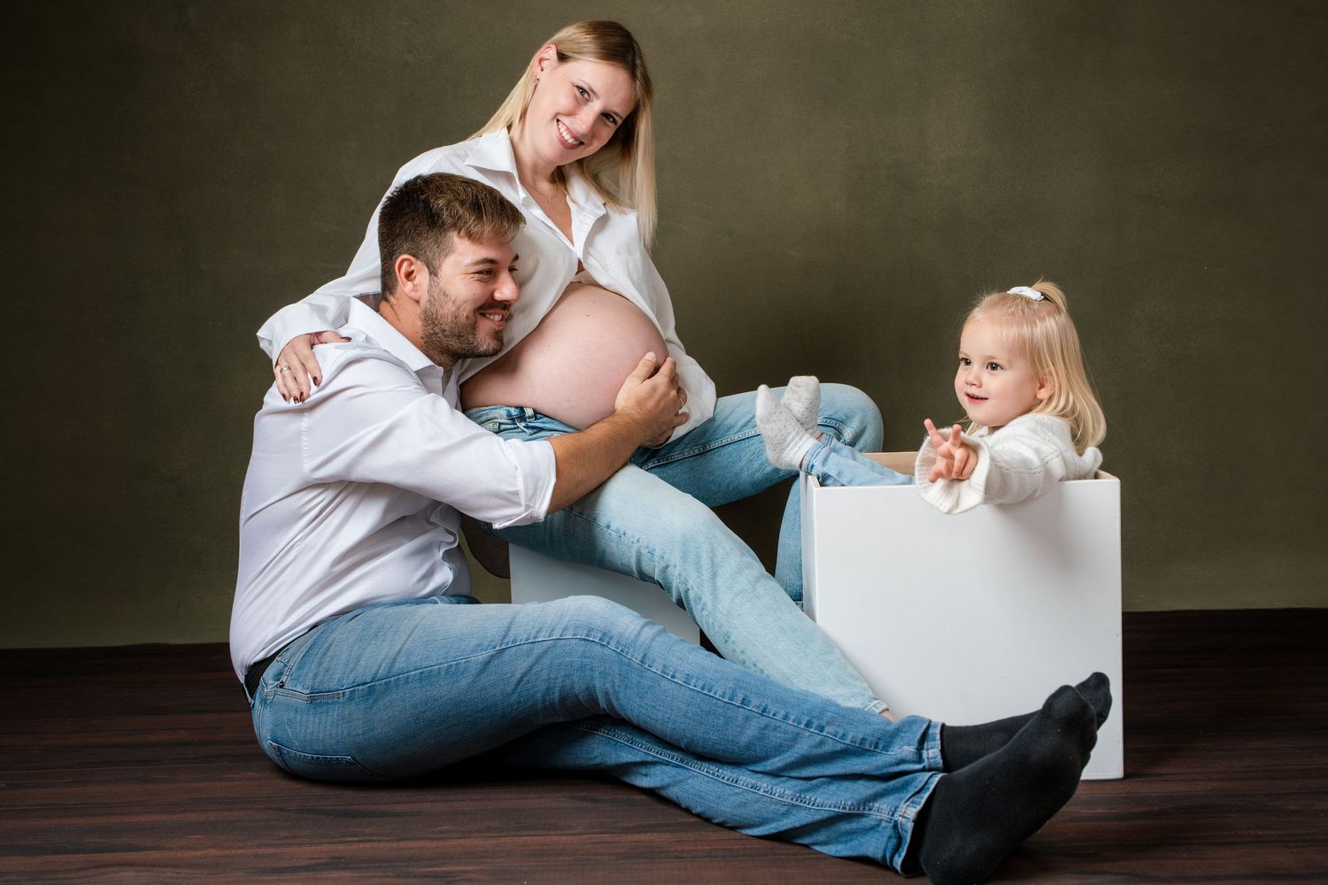 Intimate family photo session with white shirts and jeans against dark background.