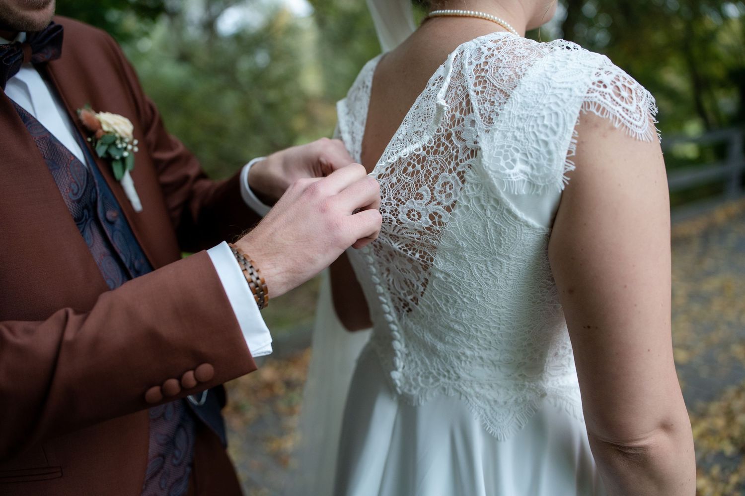 Close-up detail of lace wedding dress back with hands adjusting.