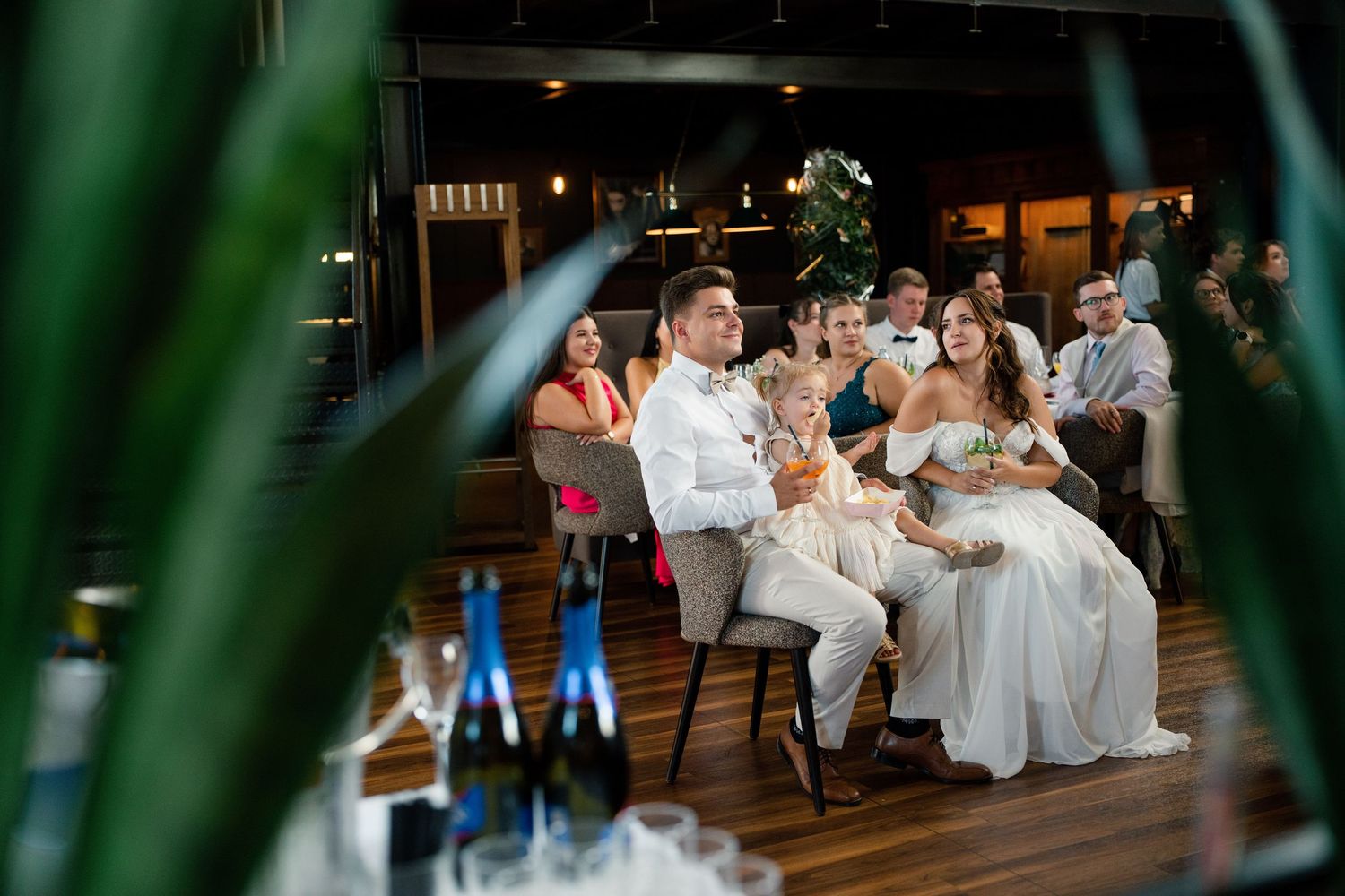 Wedding reception celebration captured through palm fronds in evening lighting.