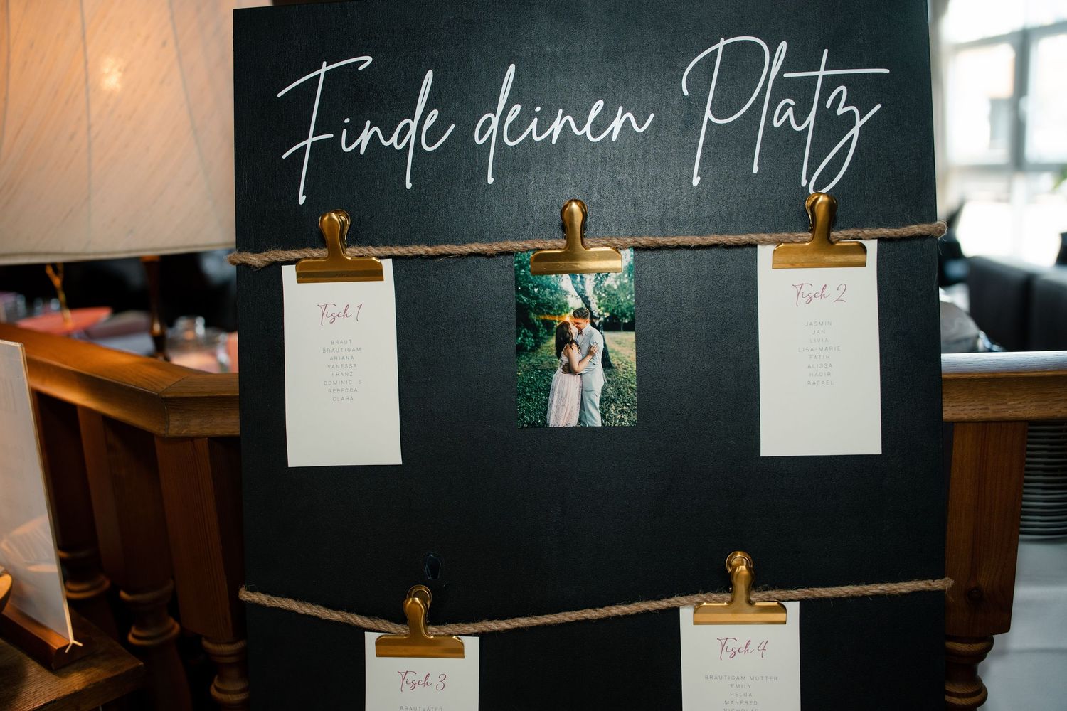 Black chalkboard seating chart display with string lights and gold clips.