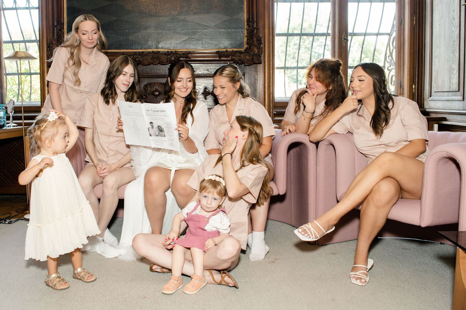 Group wearing matching robes relaxes on pink bench during pre-wedding preparations.