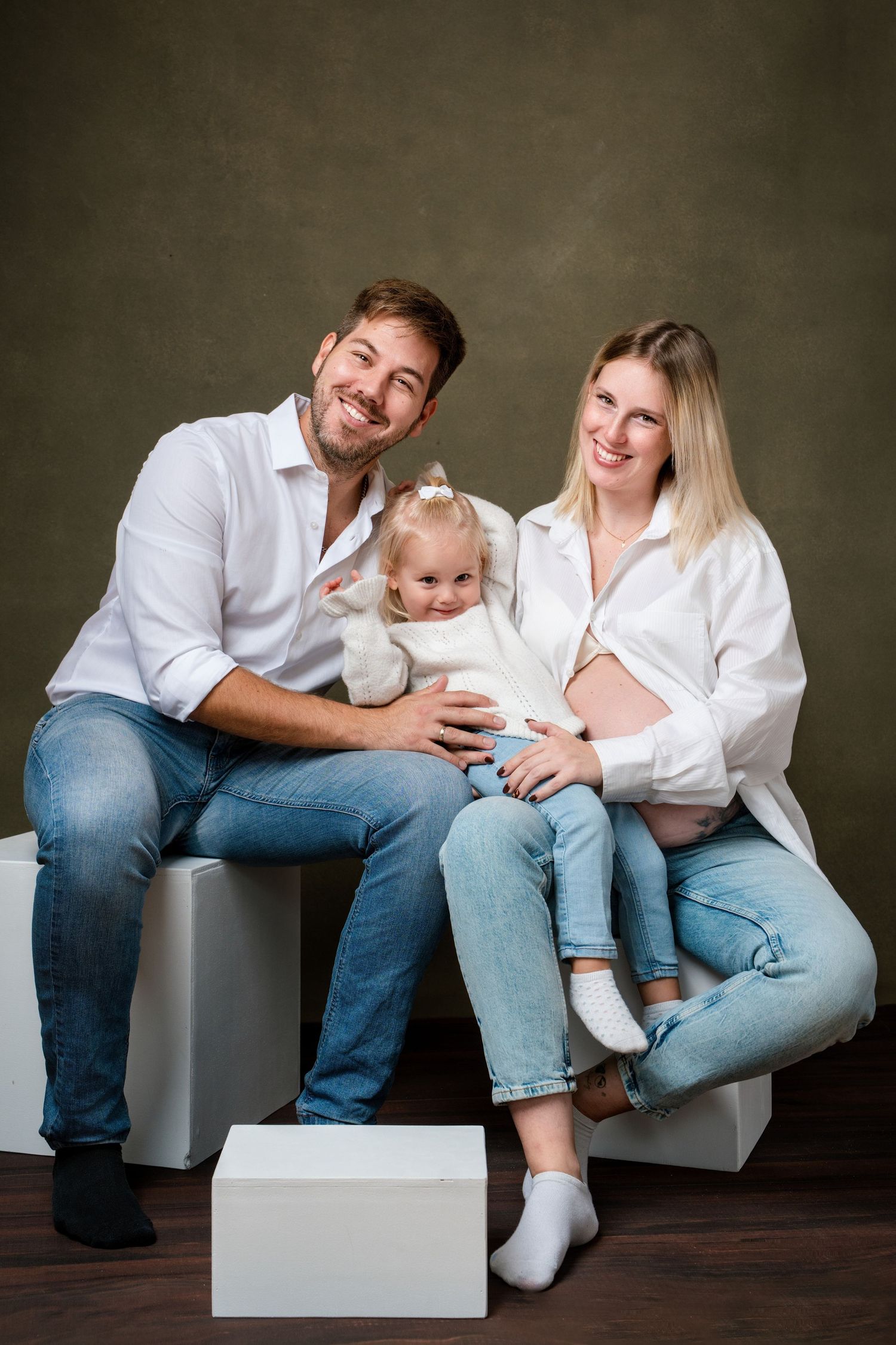 Family members sit casually on gray blocks wearing white shirts and jeans during a photo session.