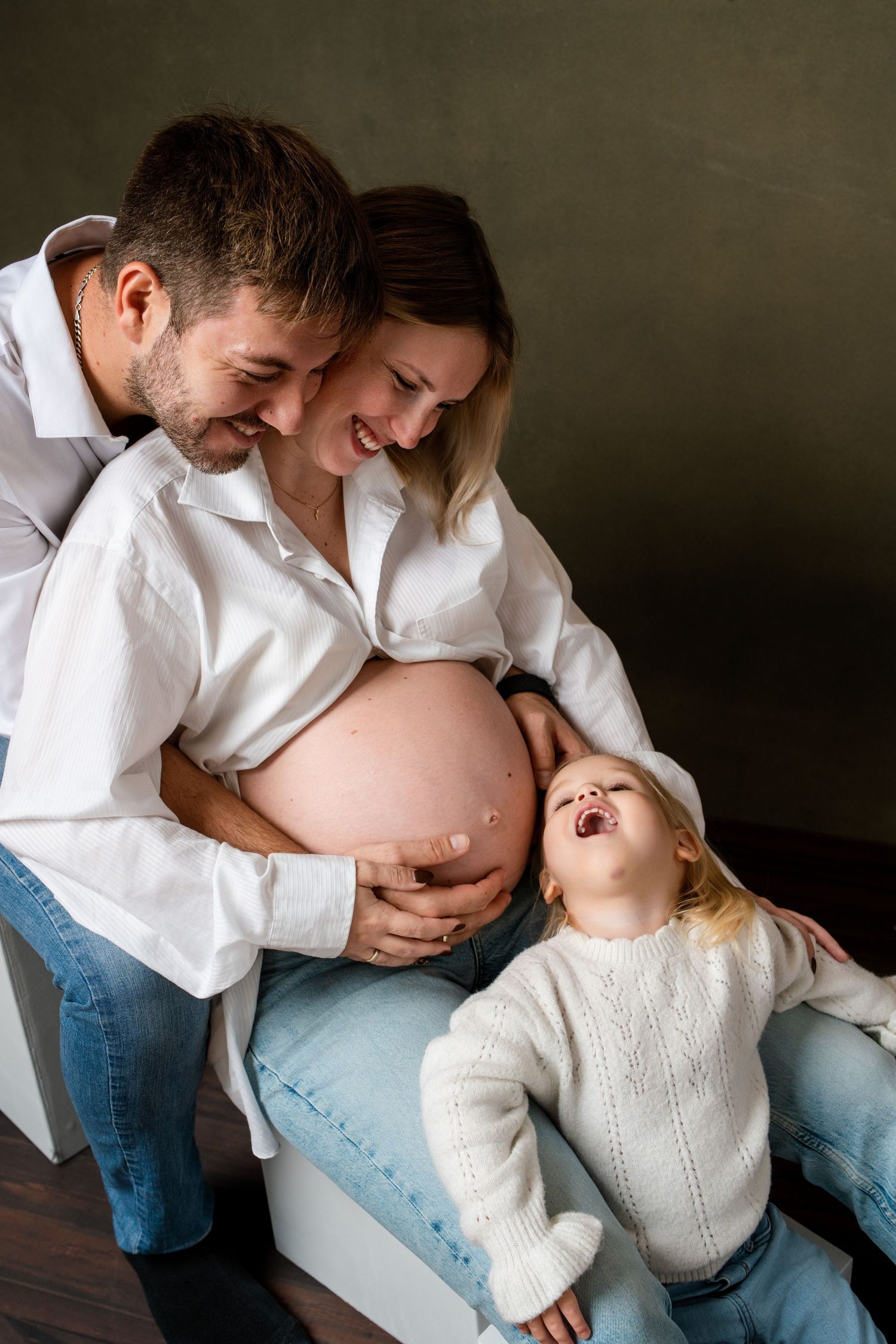 A family in white shirts and jeans shares tender moments together against a dark backdrop.