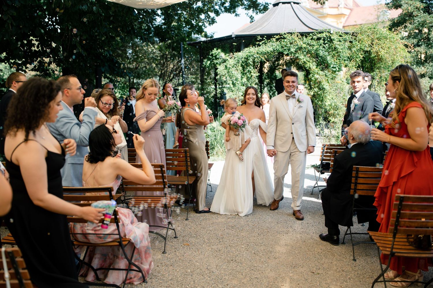 Wedding guests seated on wooden benches during an outdoor ceremony.