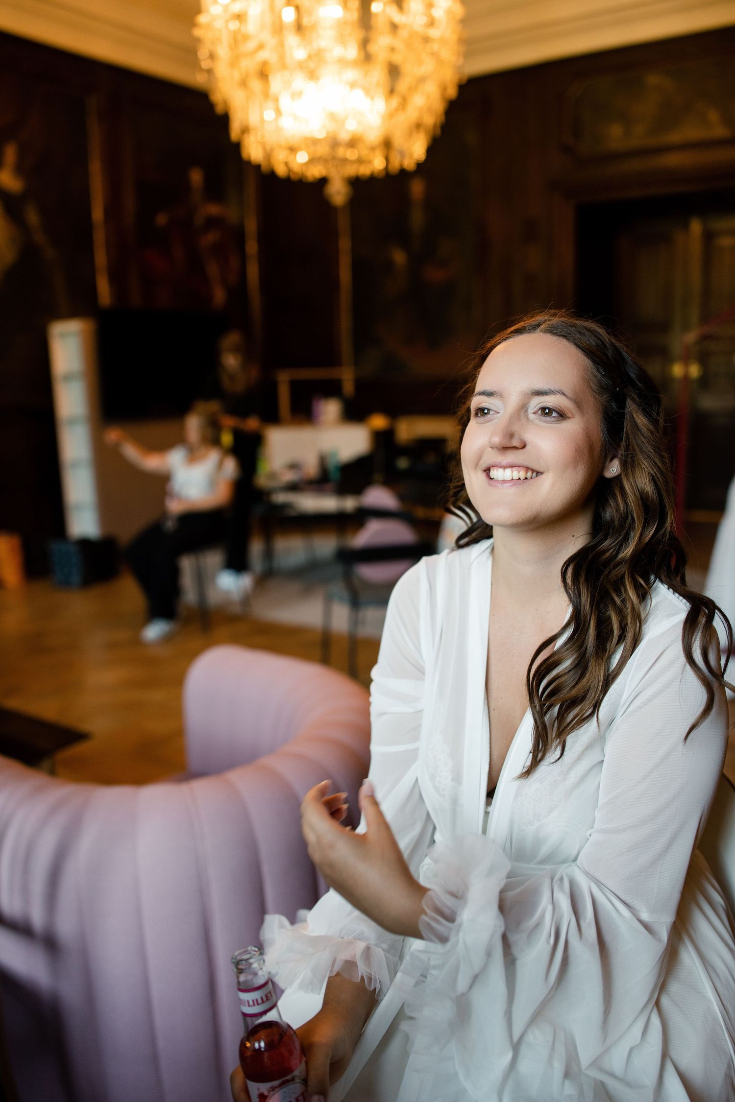 A person in a white robe sits in an elegant room with a crystal chandelier overhead.