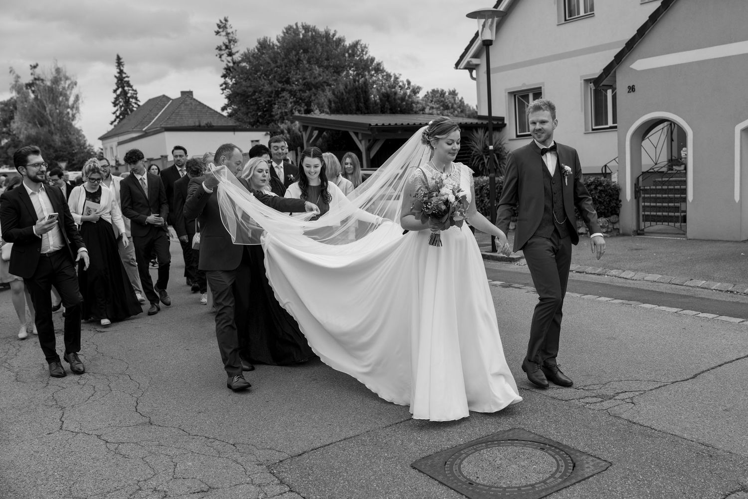 Wedding party running playfully down a street with bride's dress flowing in black and white photography.
