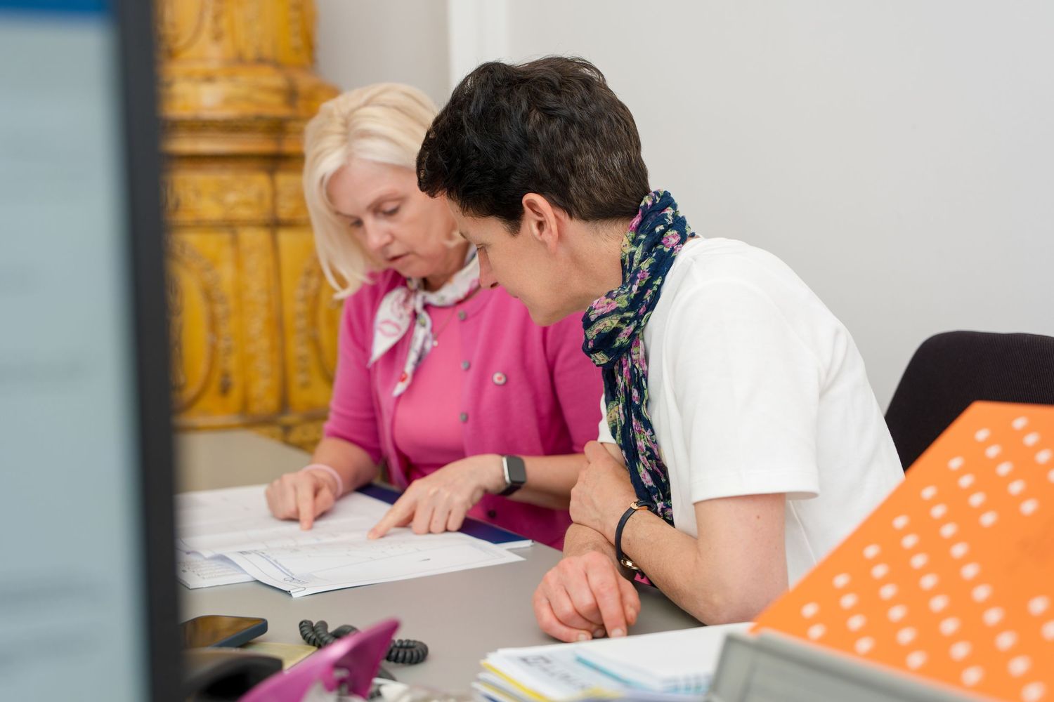 Two professional women reviewing documents together at an office desk, collaborating on paperwork.
