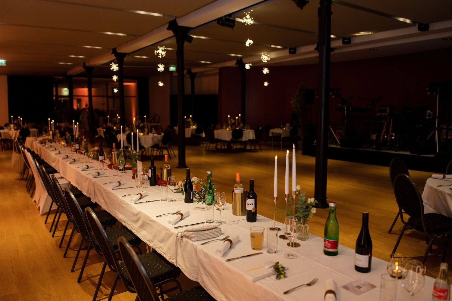 A long banquet table setup with elegant place settings and wine glasses in a dimly lit venue.