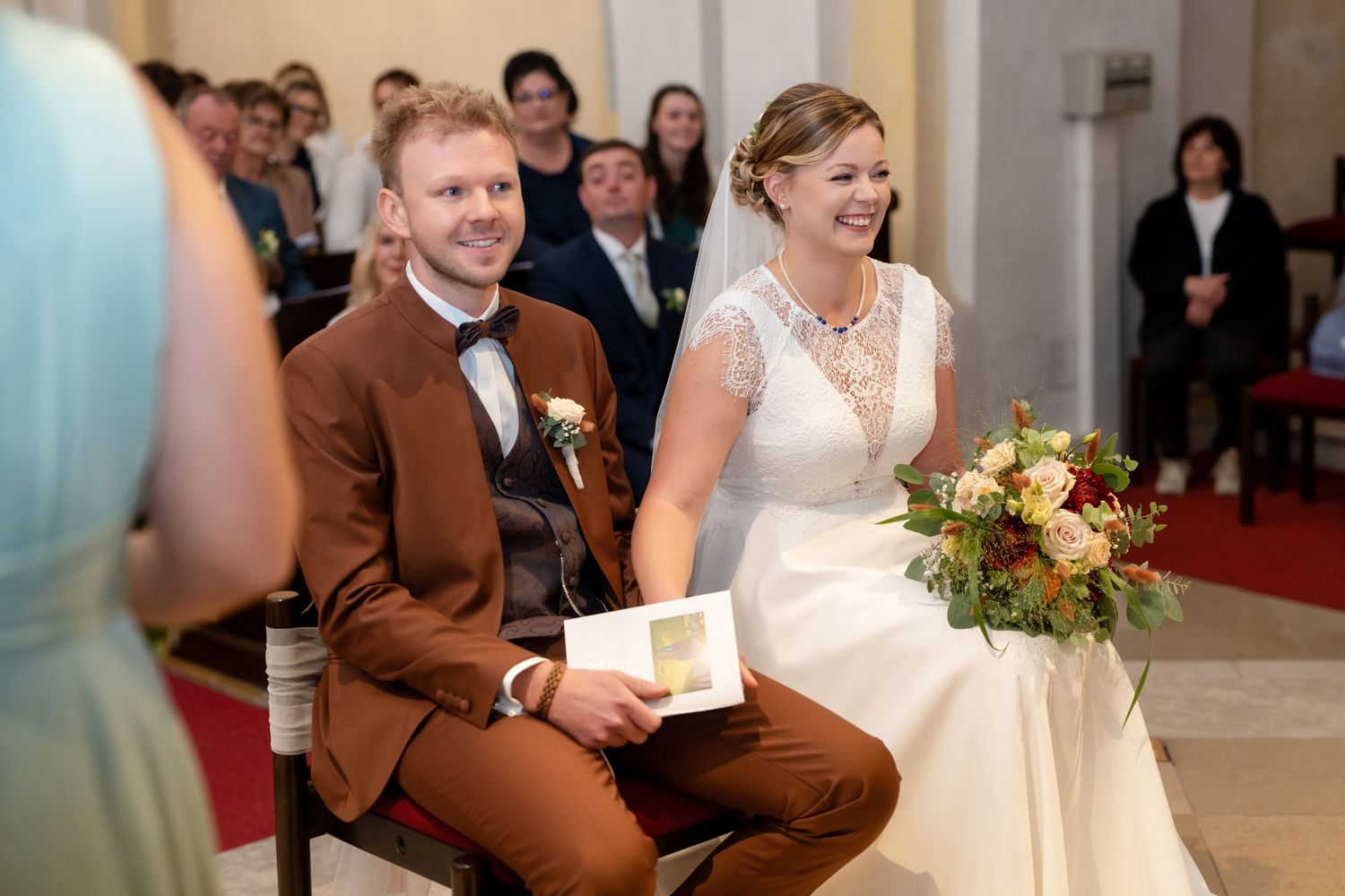 Wedding guests seated in rows at an indoor ceremony venue with warm lighting.