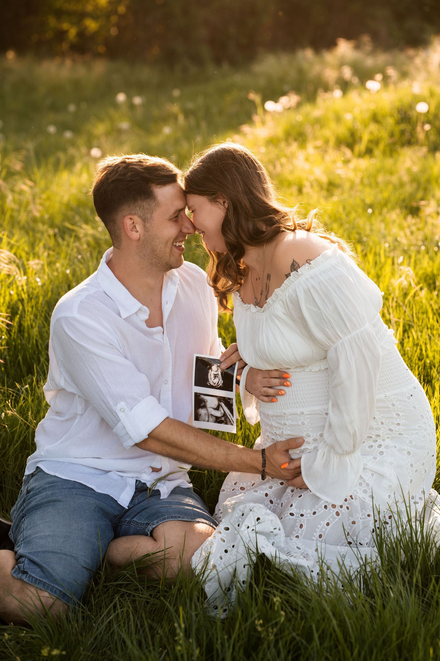 A romantic couple shares tender moments in a sunlit meadow wearing white and blue casual attire.