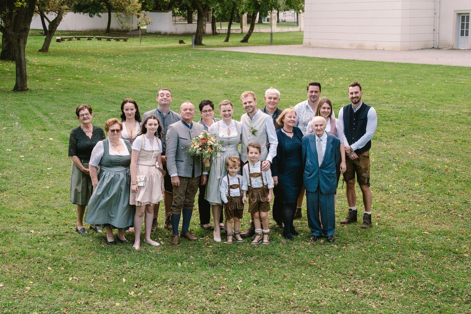 A group of wedding guests gather outdoors on a grassy lawn for a series of casual group photos.