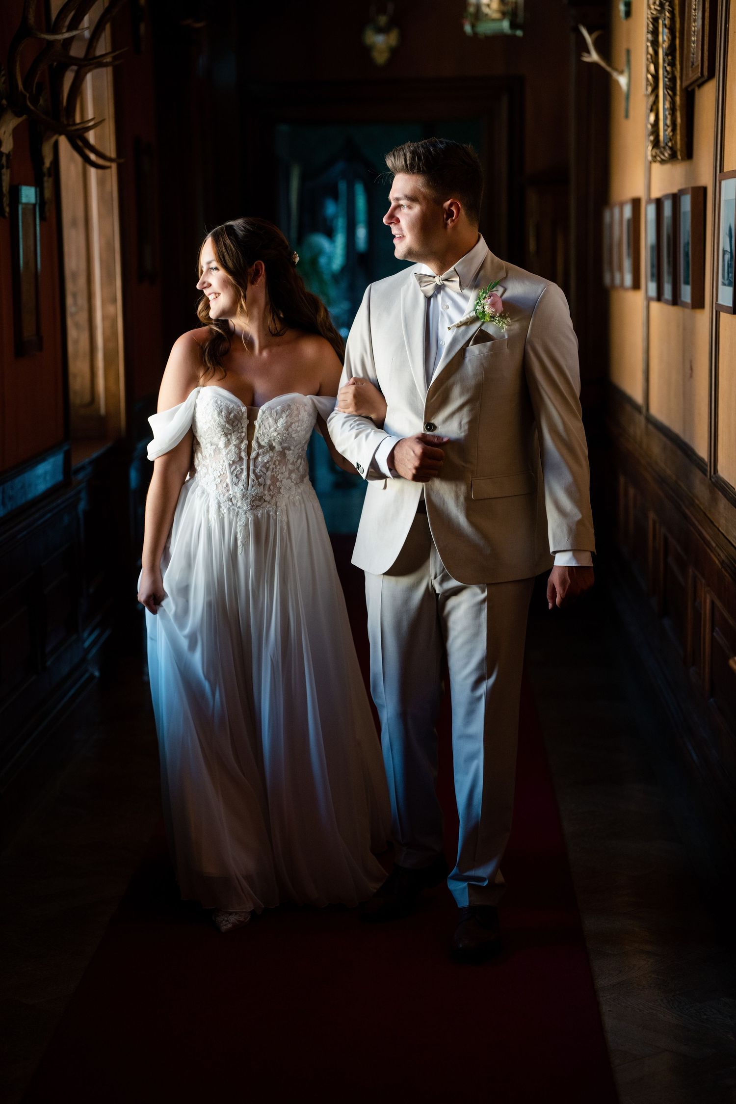 A couple in wedding attire walking through a dimly lit hallway with dramatic shadows.