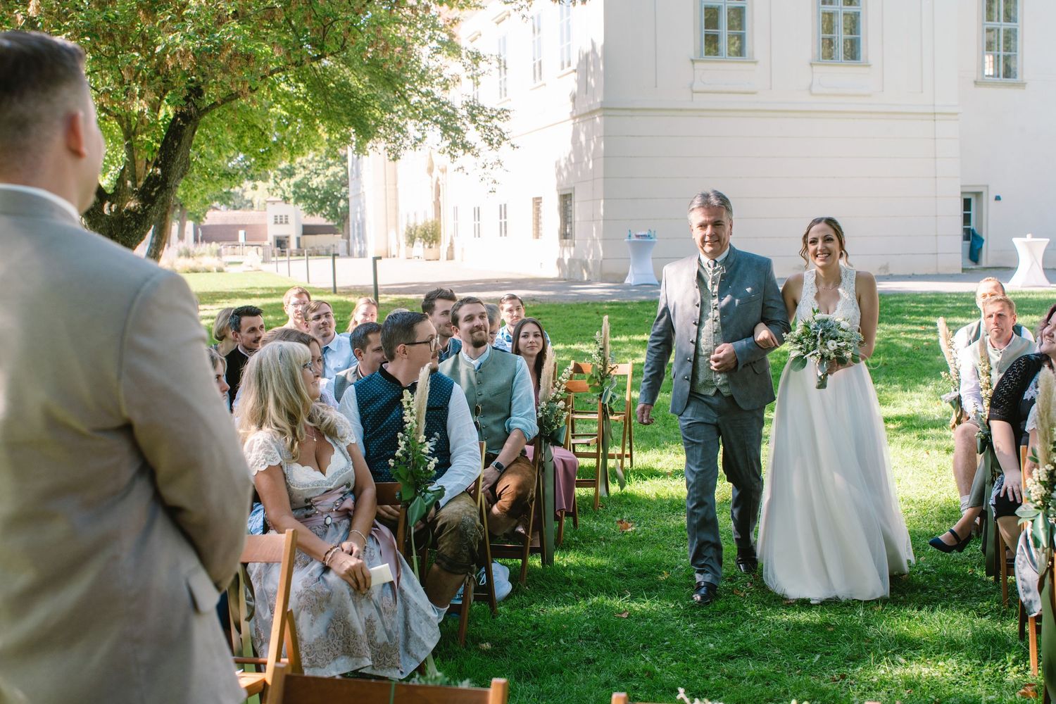 Wedding celebration in a sunny garden setting with white building in background.
