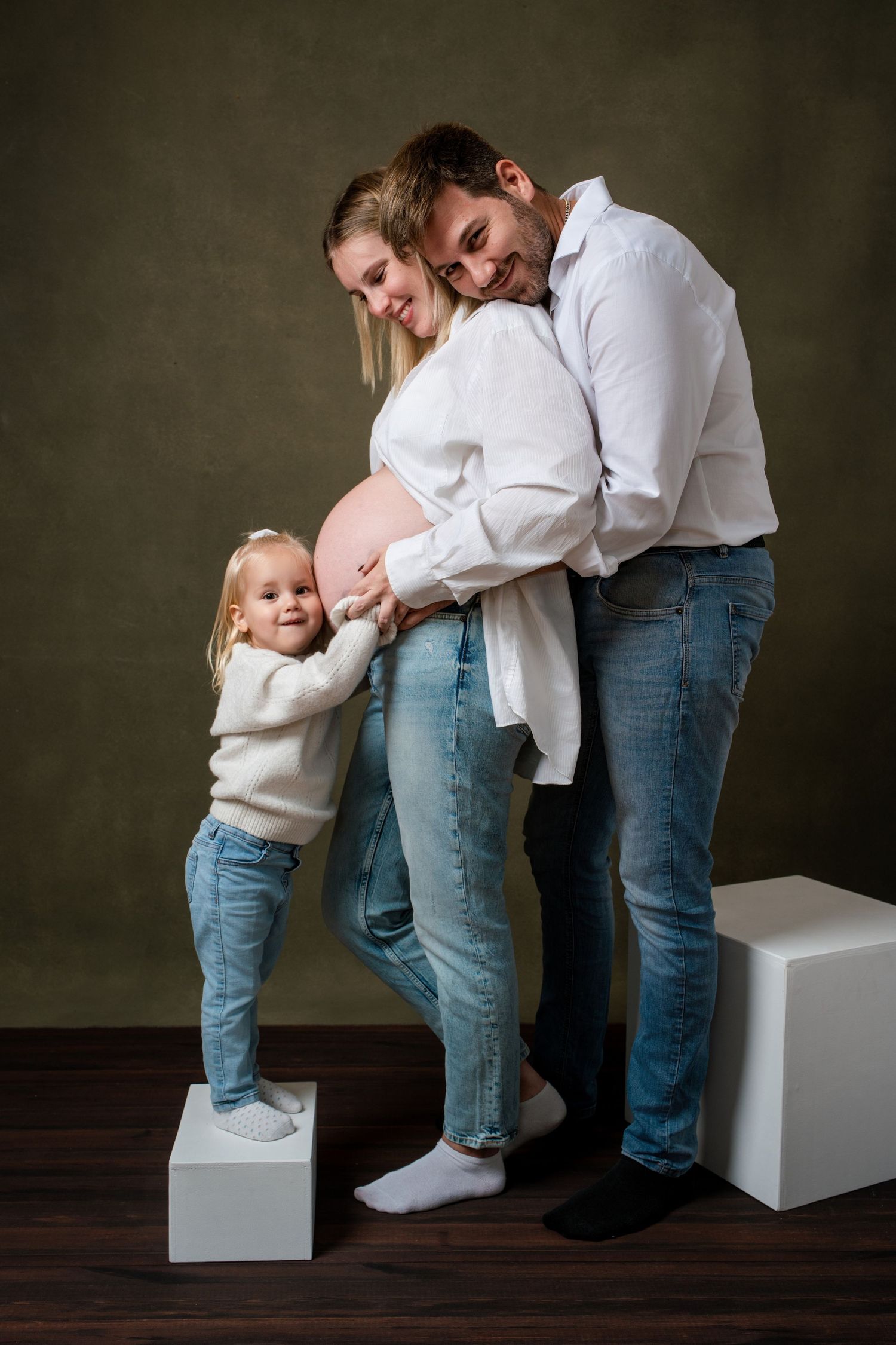 A series of intimate family photos showing playful interaction with a small child on white blocks against a dark backdrop.