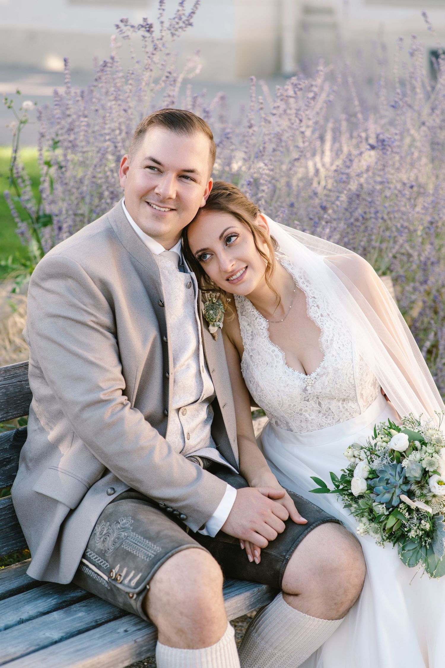 Newlyweds pose together on a garden bench surrounded by blooming lavender.