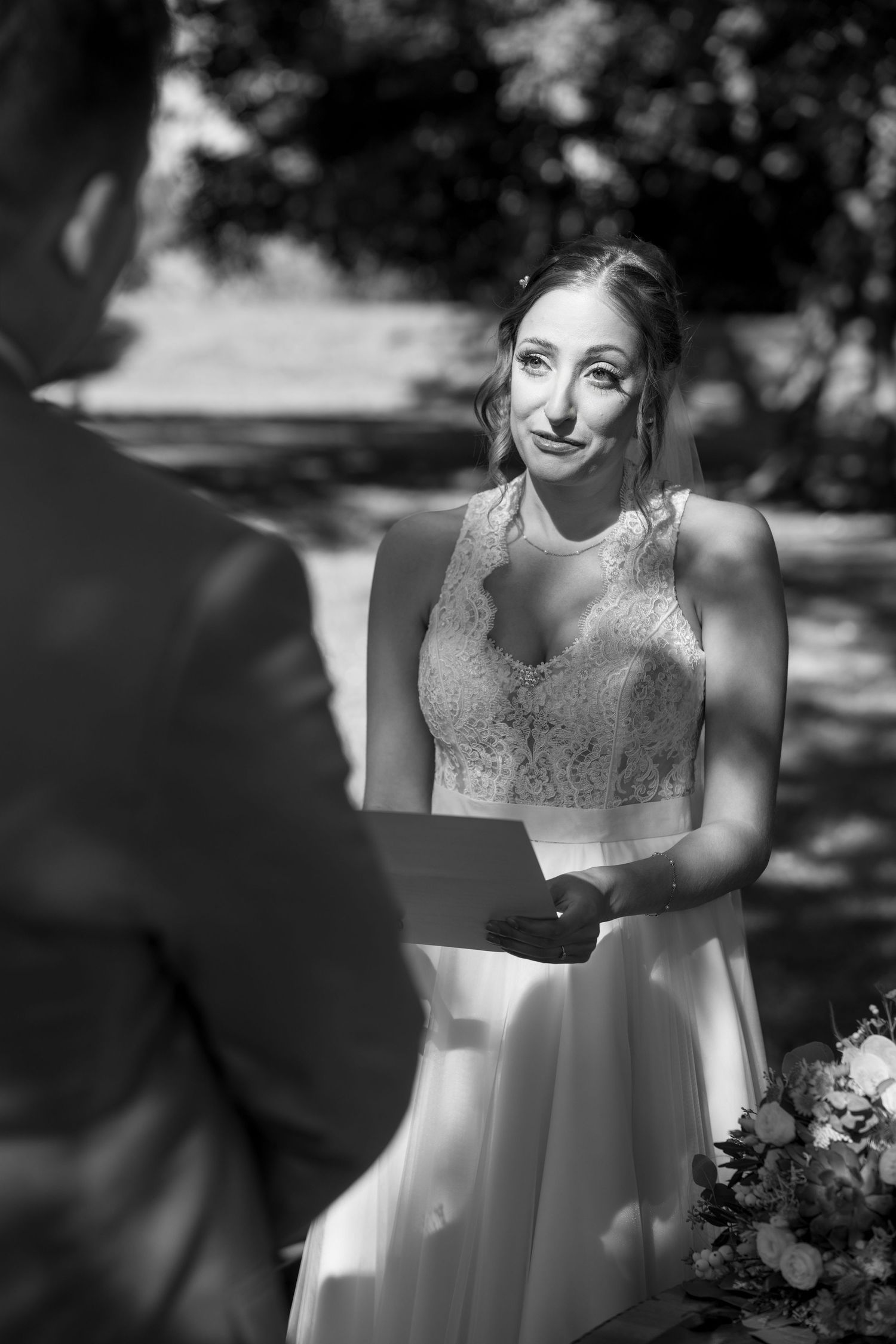 Black and white portrait of a bride in a lace wedding dress smiling in natural sunlight.