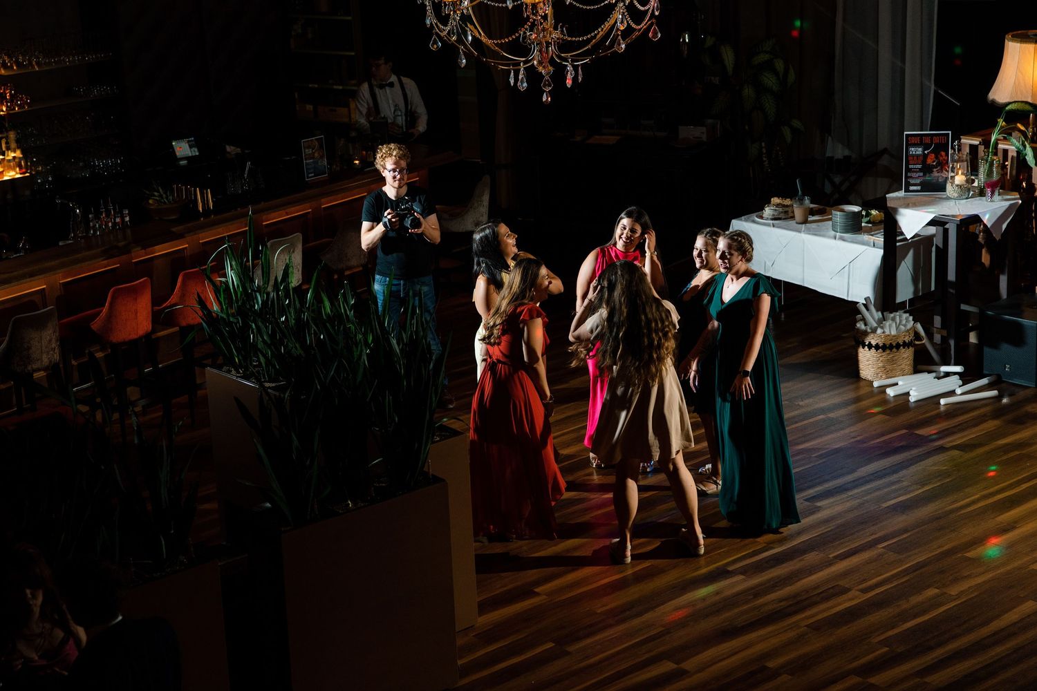 Wedding guests dancing on a wooden floor under a chandelier during an evening reception.
