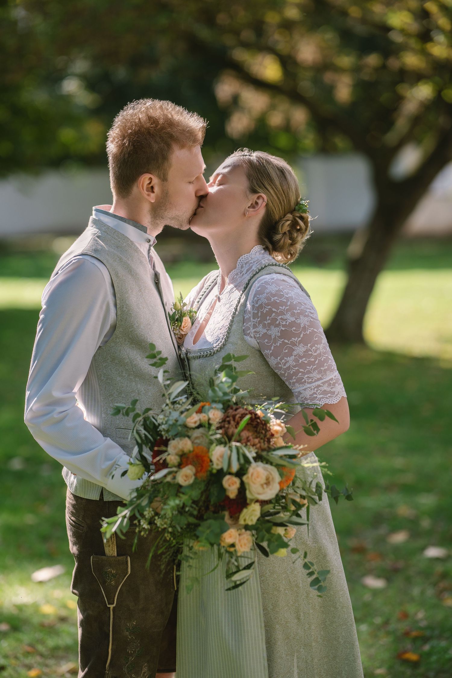 A romantic wedding couple embraces outdoors in autumn with a rustic bouquet featuring peach and cream flowers.