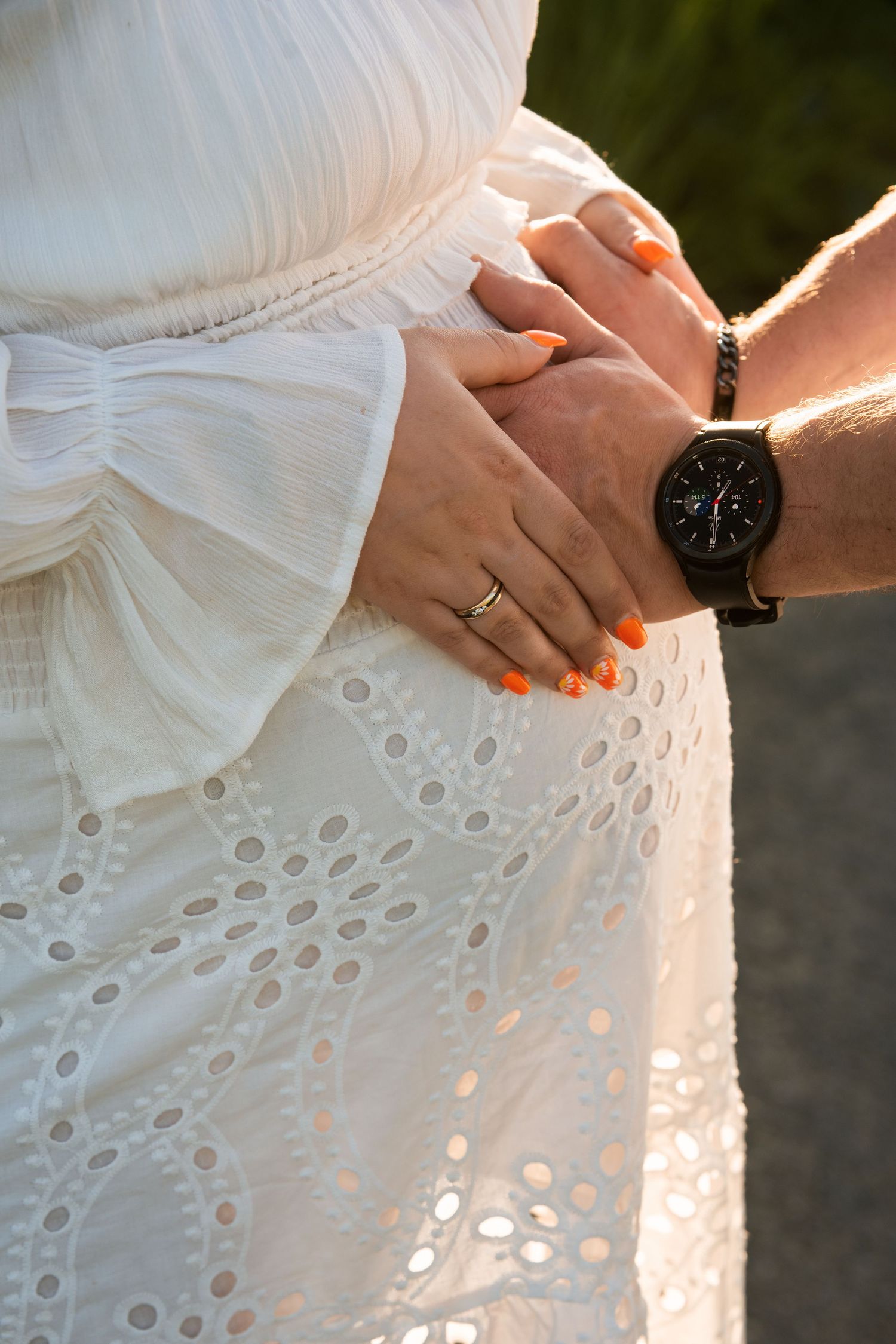 Close-up shots of hands wearing wedding rings against white eyelet lace fabric in golden sunlight.