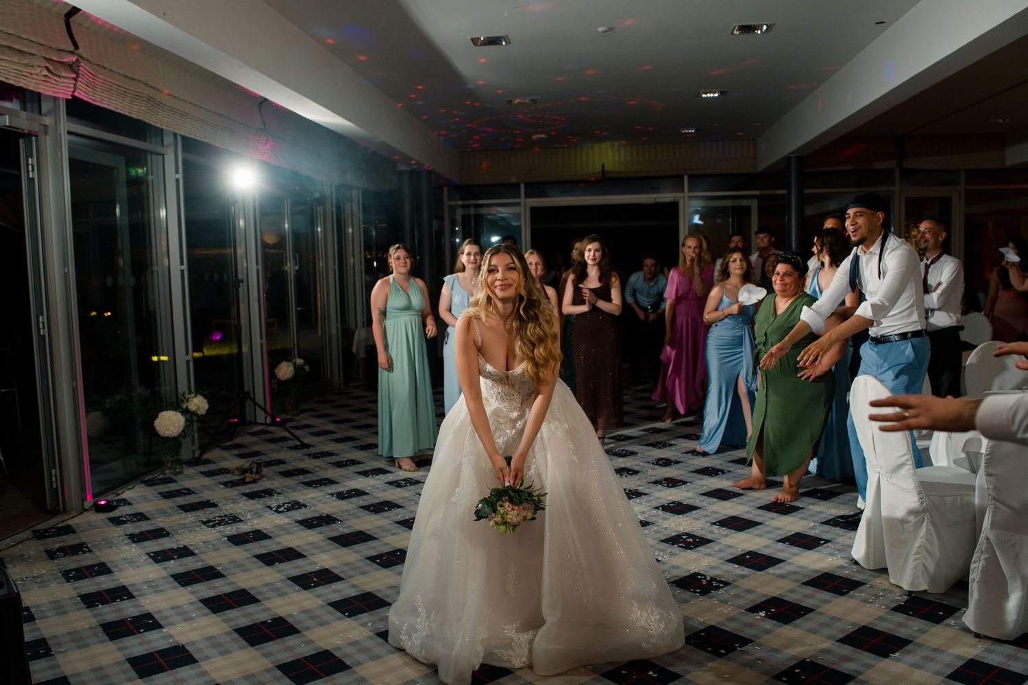 Bride preparing to toss bouquet to guests at elegant wedding reception on checkered dance floor.