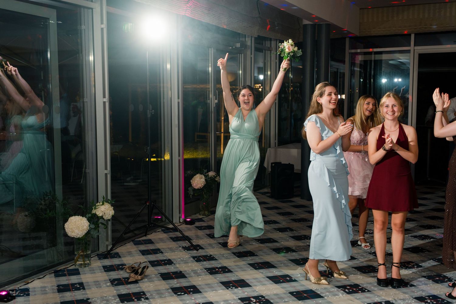 Women celebrating bouquet toss at wedding reception on checkered dance floor.