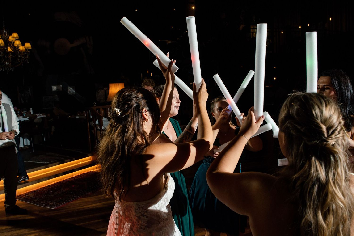 Wedding guests raise illuminated foam sticks in celebration on the dance floor.