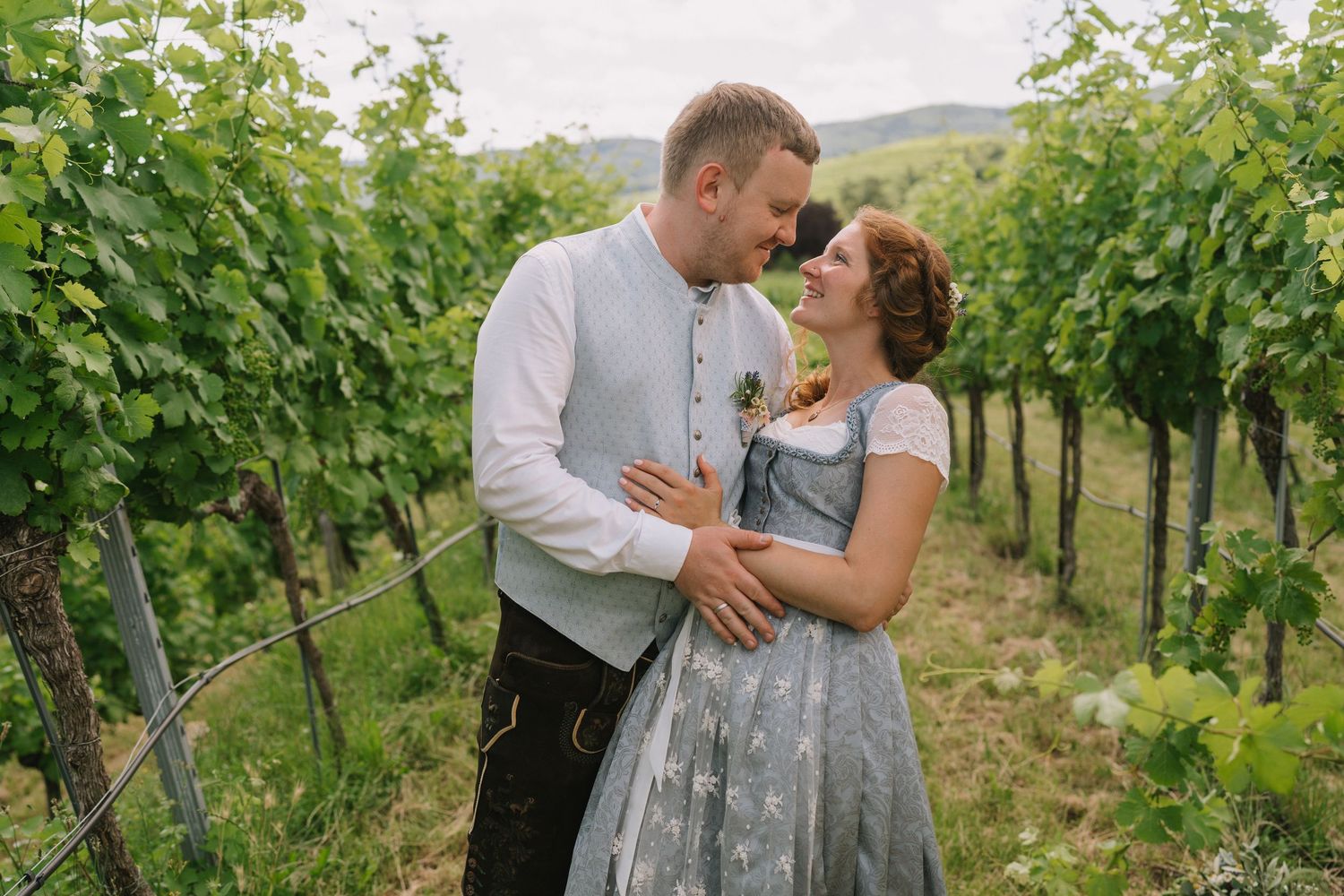 Romantic couple embracing in sunny vineyard with green grapevines.