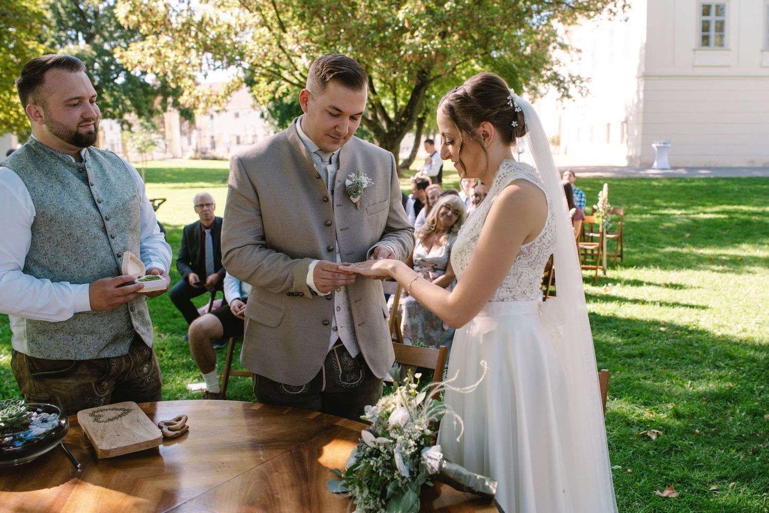 Outdoor wedding celebration with guests gathered on a lawn near a white building.