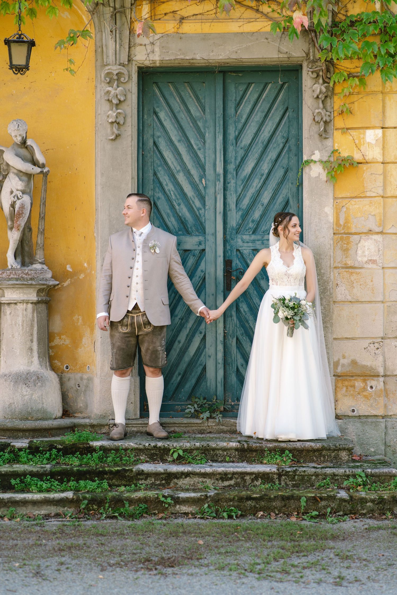 Wedding couple poses in front of a historic yellow building with teal doors.