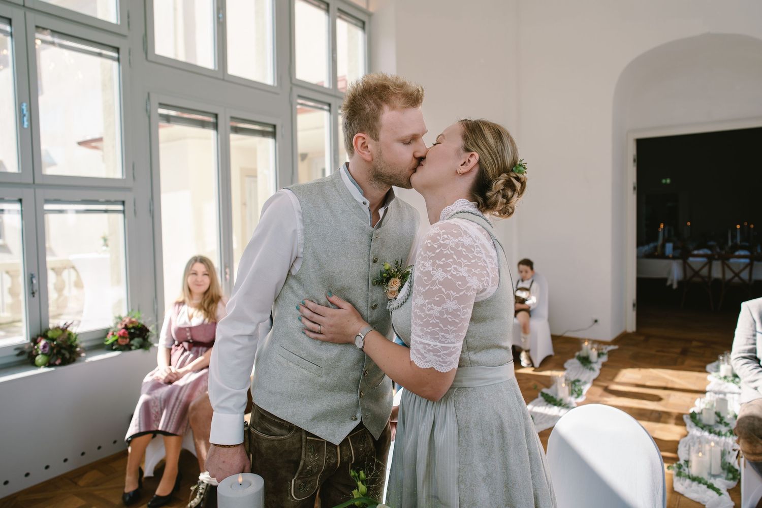 A couple embraces in a bright, sunlit room with white walls during an intimate wedding celebration.