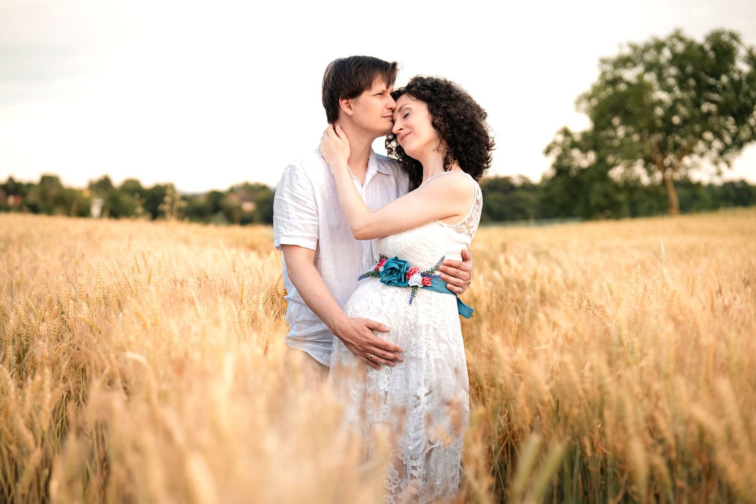 A romantic couple embraces in a golden wheat field at sunset creating a dreamy summer portrait.