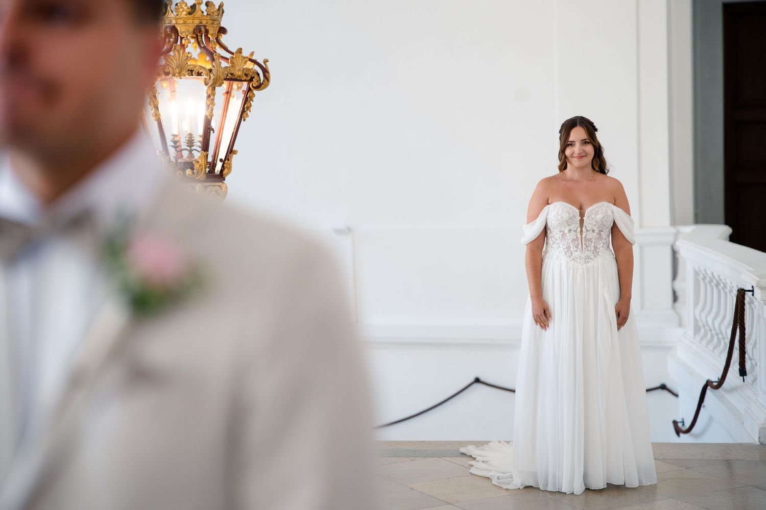Wedding couple standing in elegant white interior with chandelier.