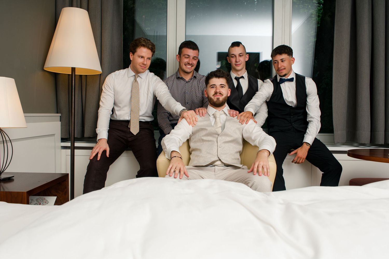 Groom and groomsmen posing together in a hotel room, smiling and celebrating before the wedding ceremony.