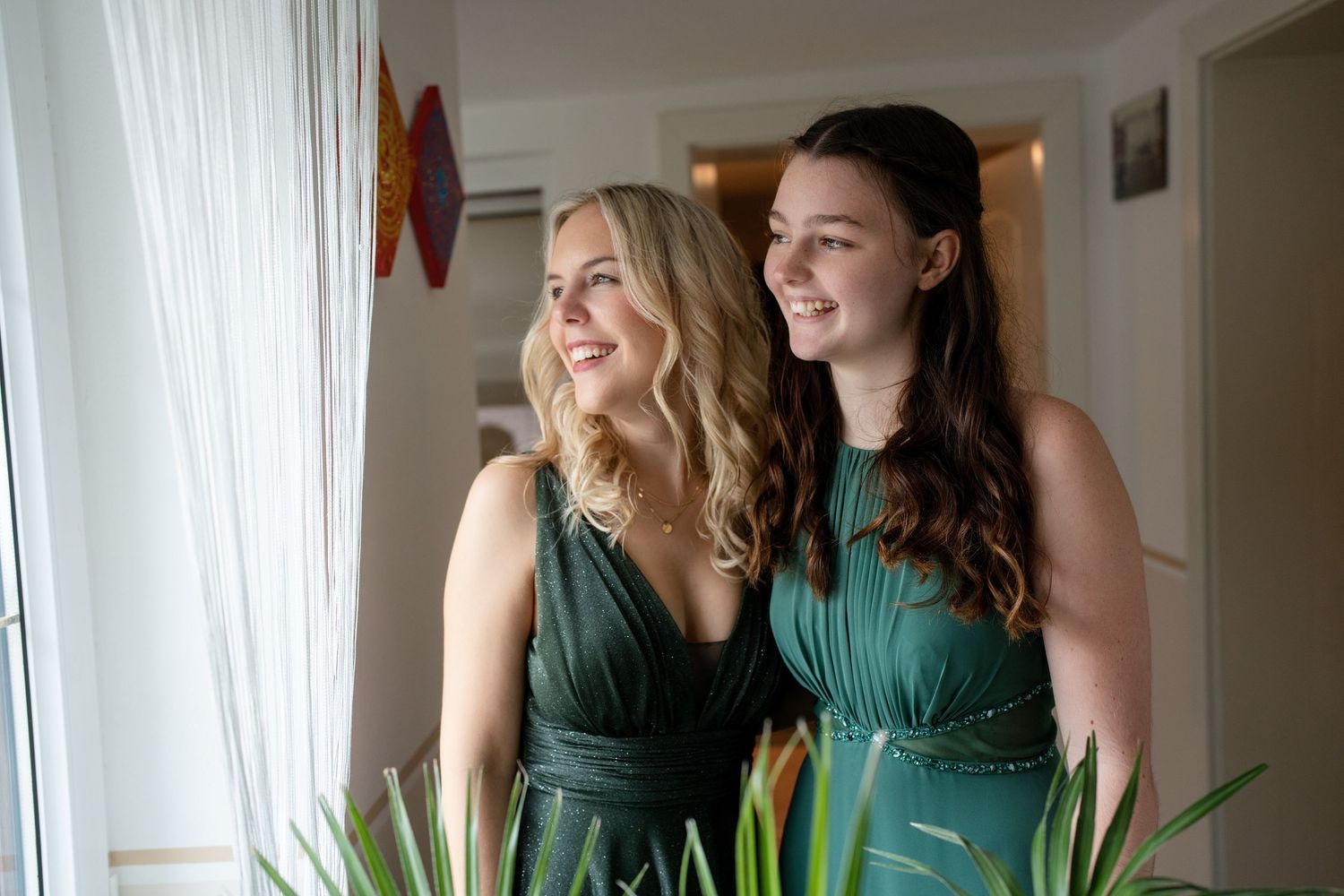 Two women in matching green dresses share a candid moment in a bright room.