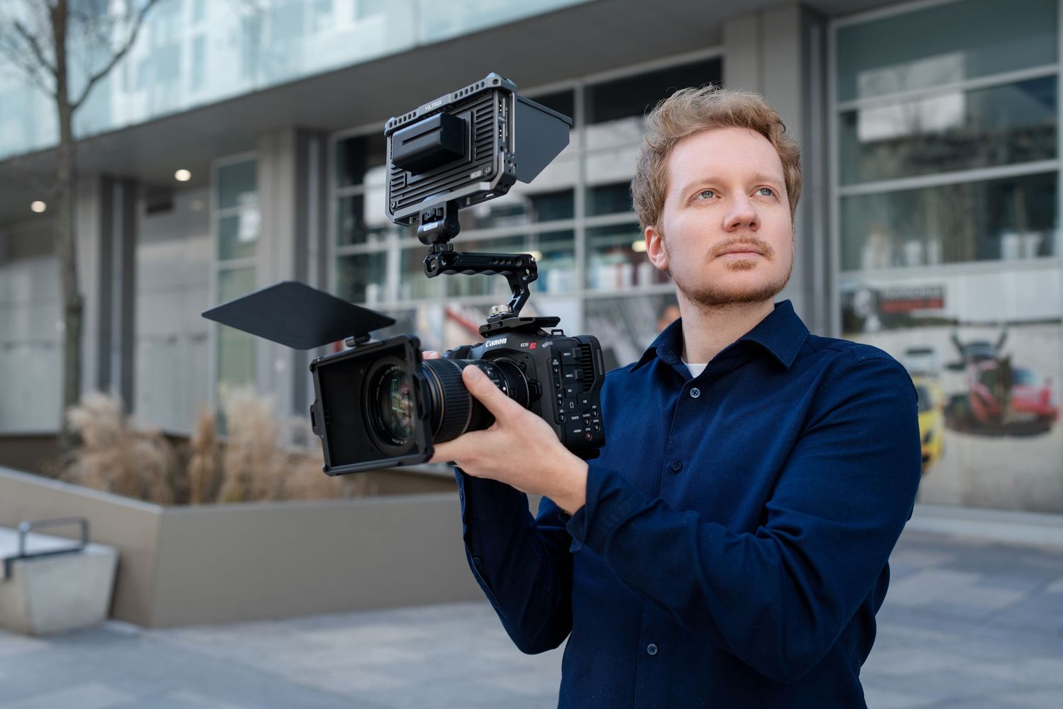 Photographer in navy blue jacket holding professional video camera outdoors.