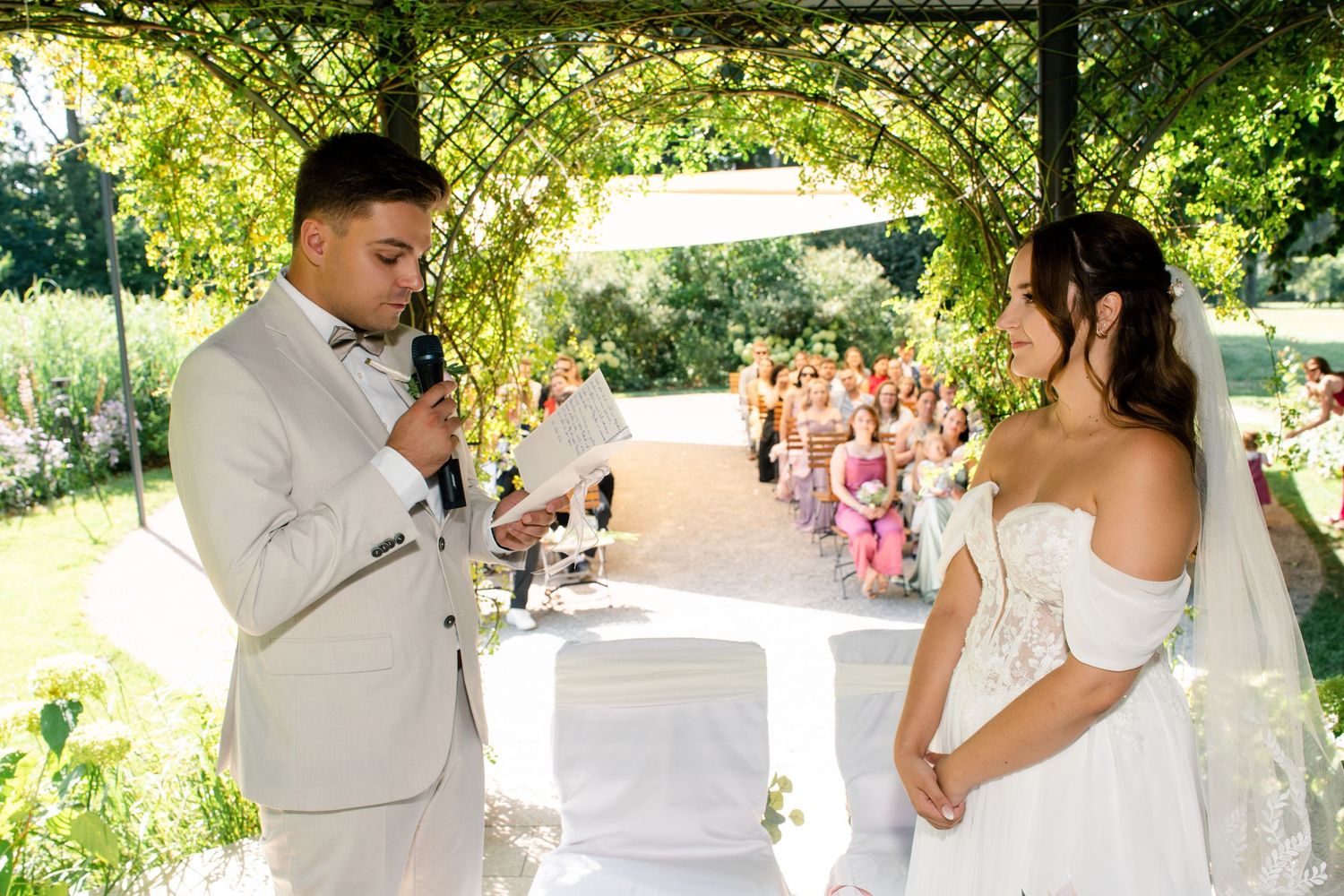 Wedding ceremony taking place under a natural green canopy of trees.