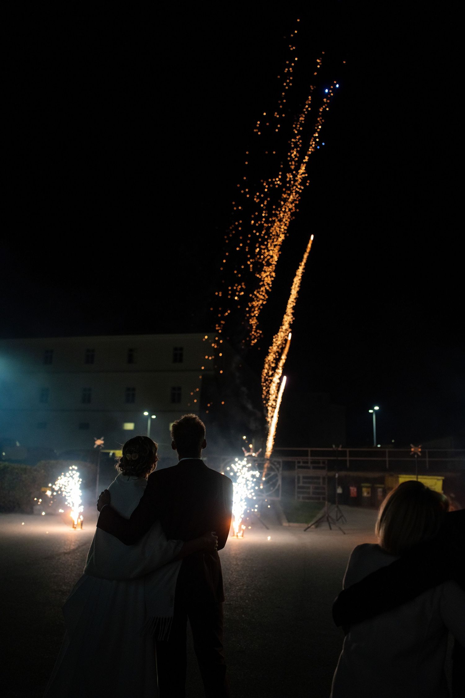 Silhouettes of people watching fireworks display against a dark night sky with bright sparkling effects.