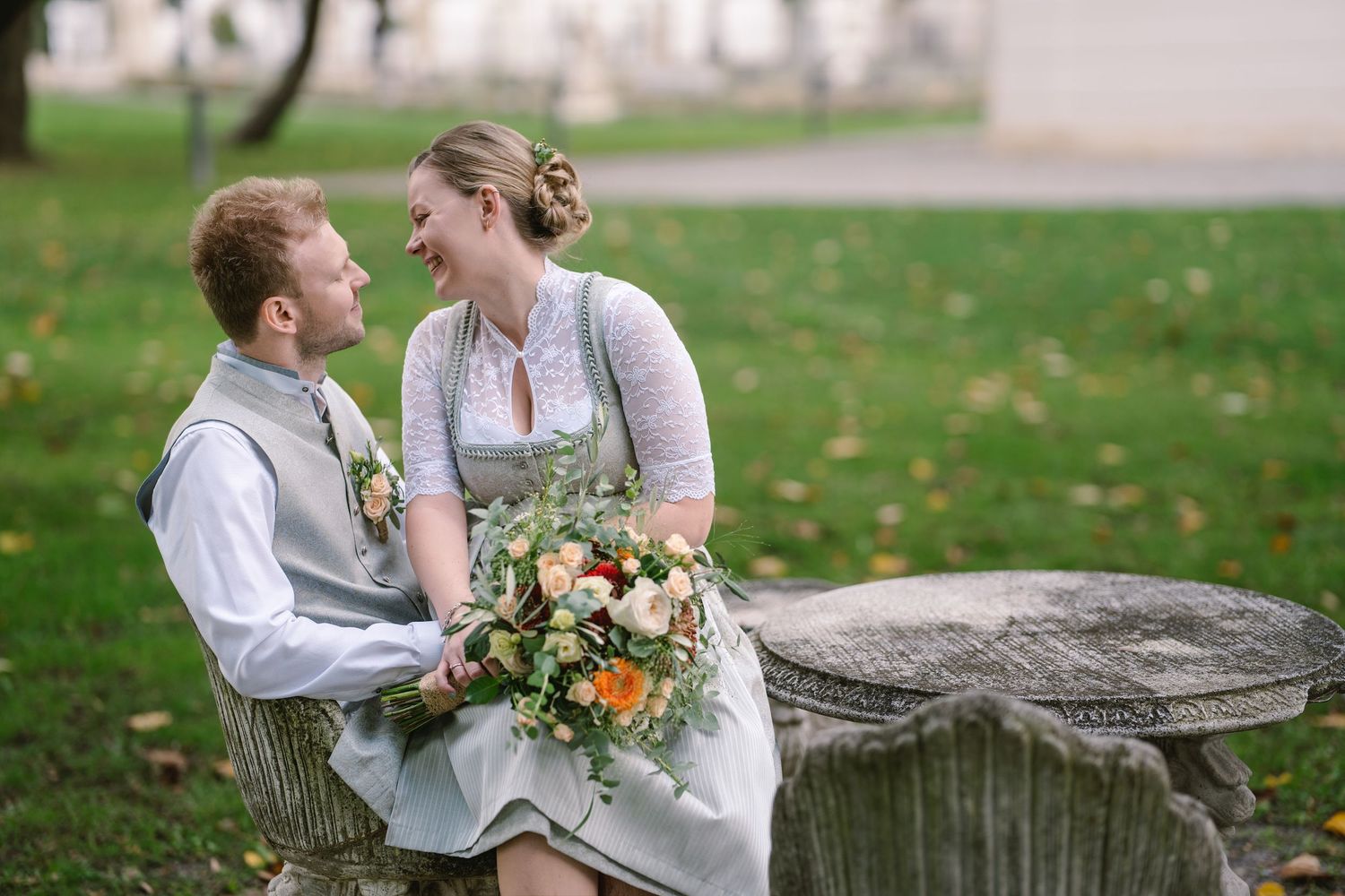 A romantic outdoor photoshoot in a park with a couple wearing vintage-inspired clothing and holding flowers.