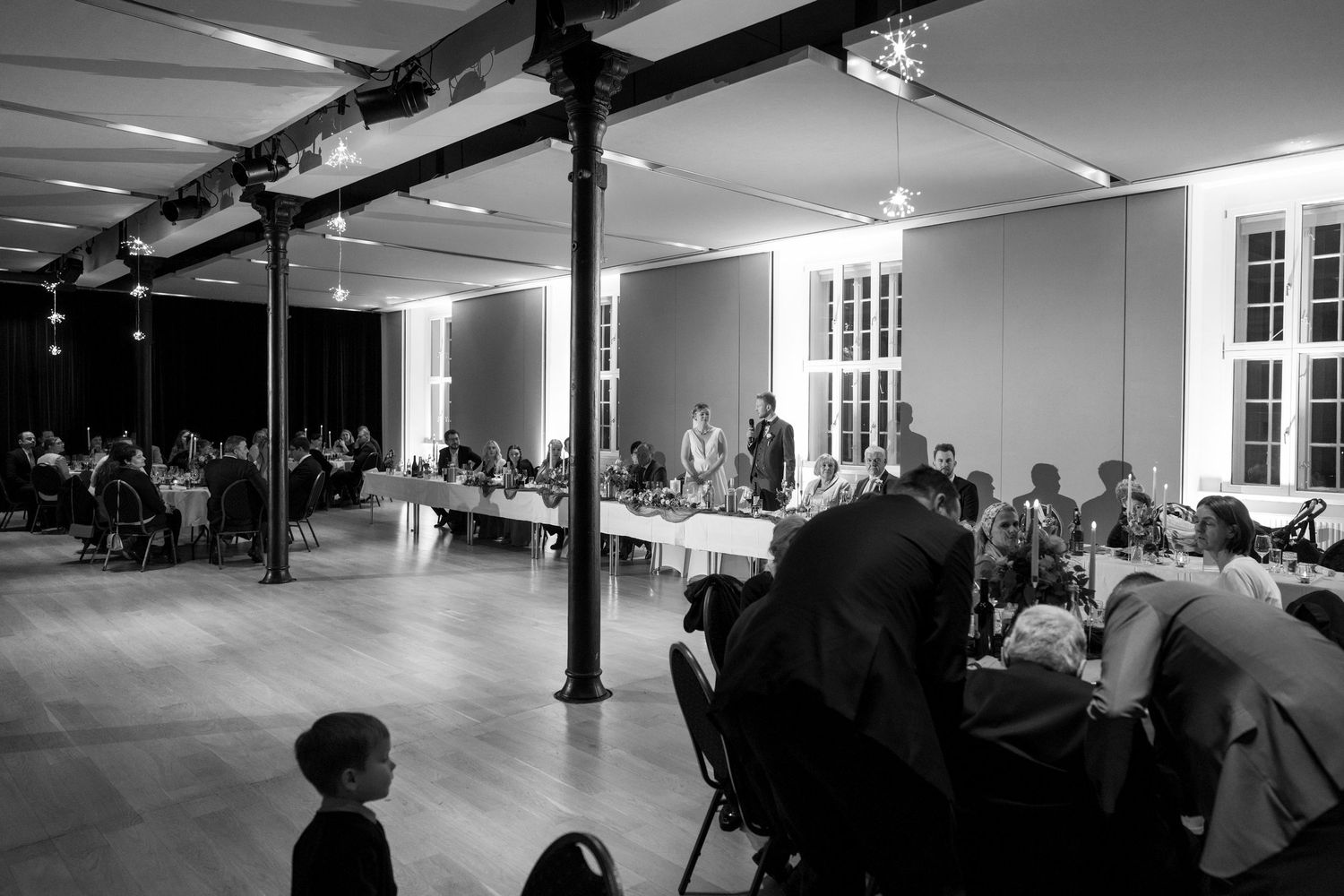 Black and white interior view of a large dance studio space with exposed beams and windows.