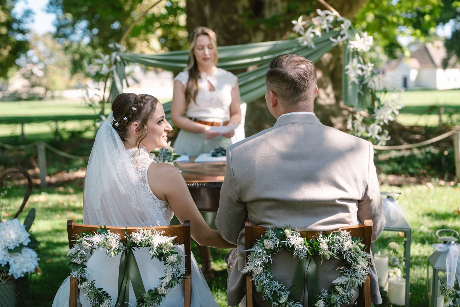 Wedding party seated at decorated tables in lush garden setting.