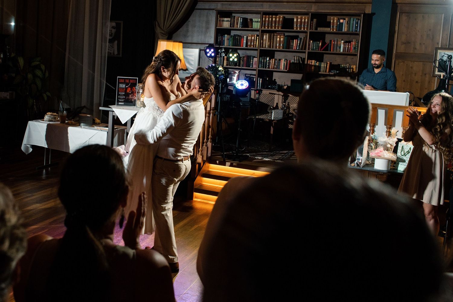 A couple shares their first dance at a wedding reception in a library-themed venue with bookshelves in the background.