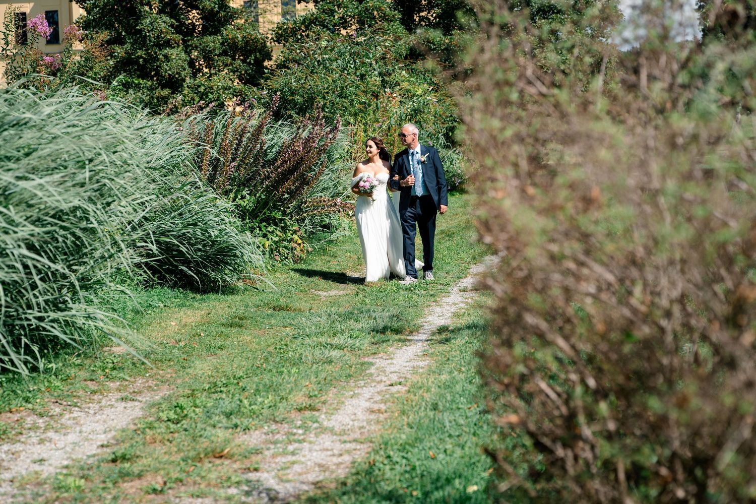 Wedding party members walk along scenic garden pathway.