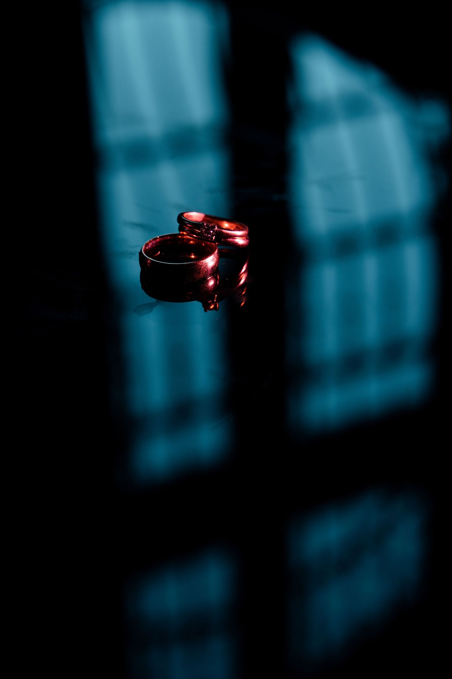 Wedding rings cast dramatic shadows in moody blue lighting.