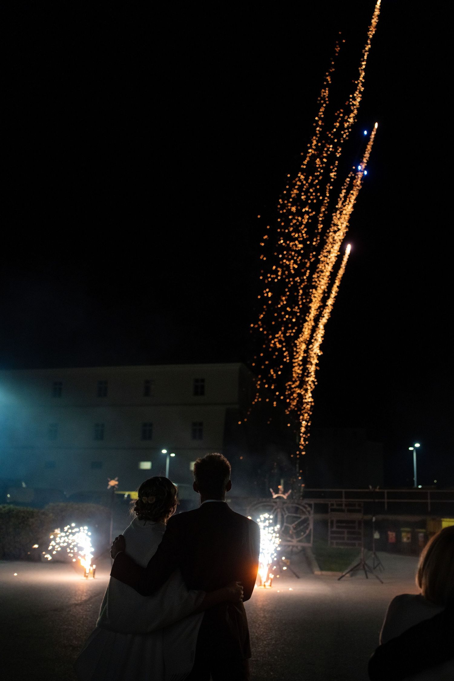 Silhouettes watch golden fireworks display against dark night sky.