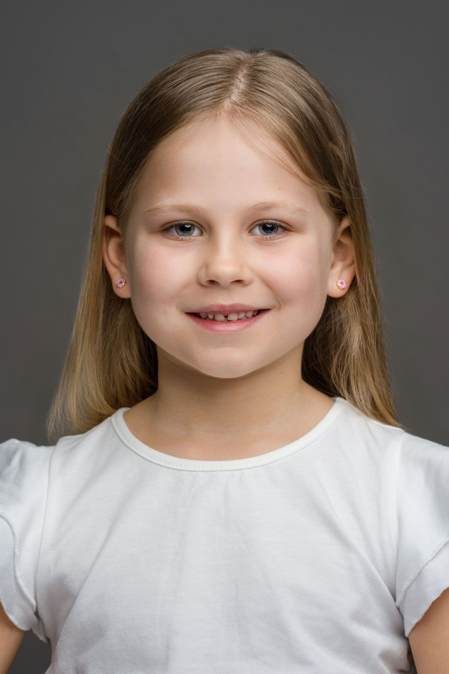 Young child wearing a white shirt against a gray background with a cheerful expression.