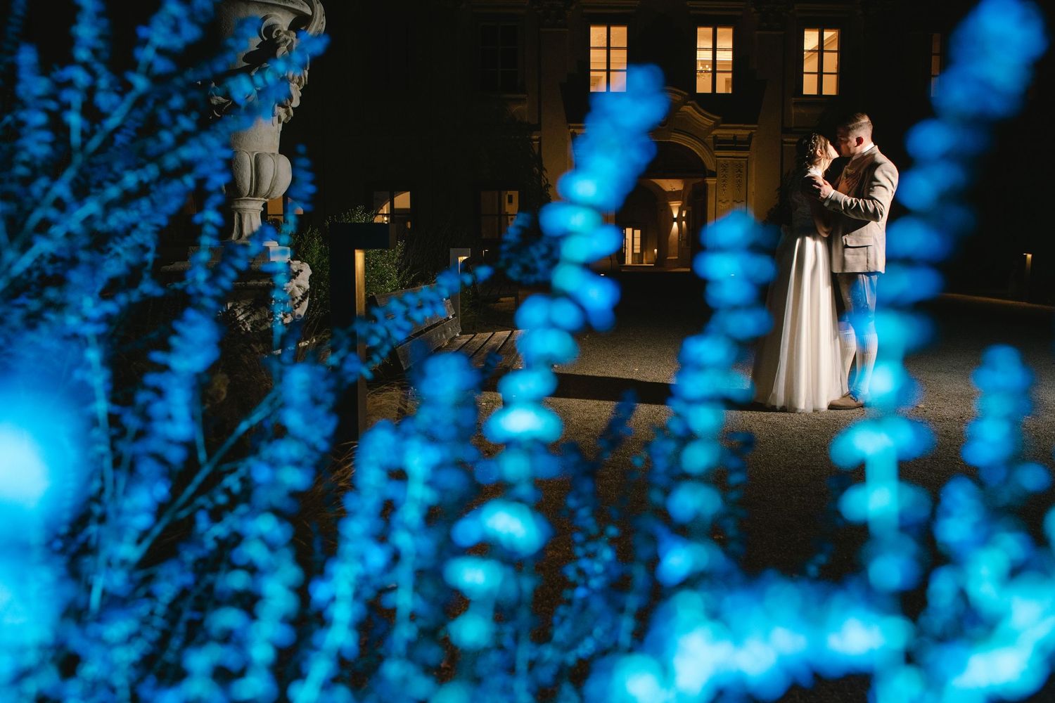 Illuminated windows glow warmly against dark building facade with silhouettes in foreground.