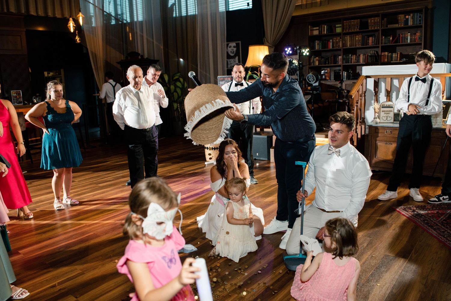 Wedding reception guests dancing and celebrating on a wooden dance floor under warm lighting.