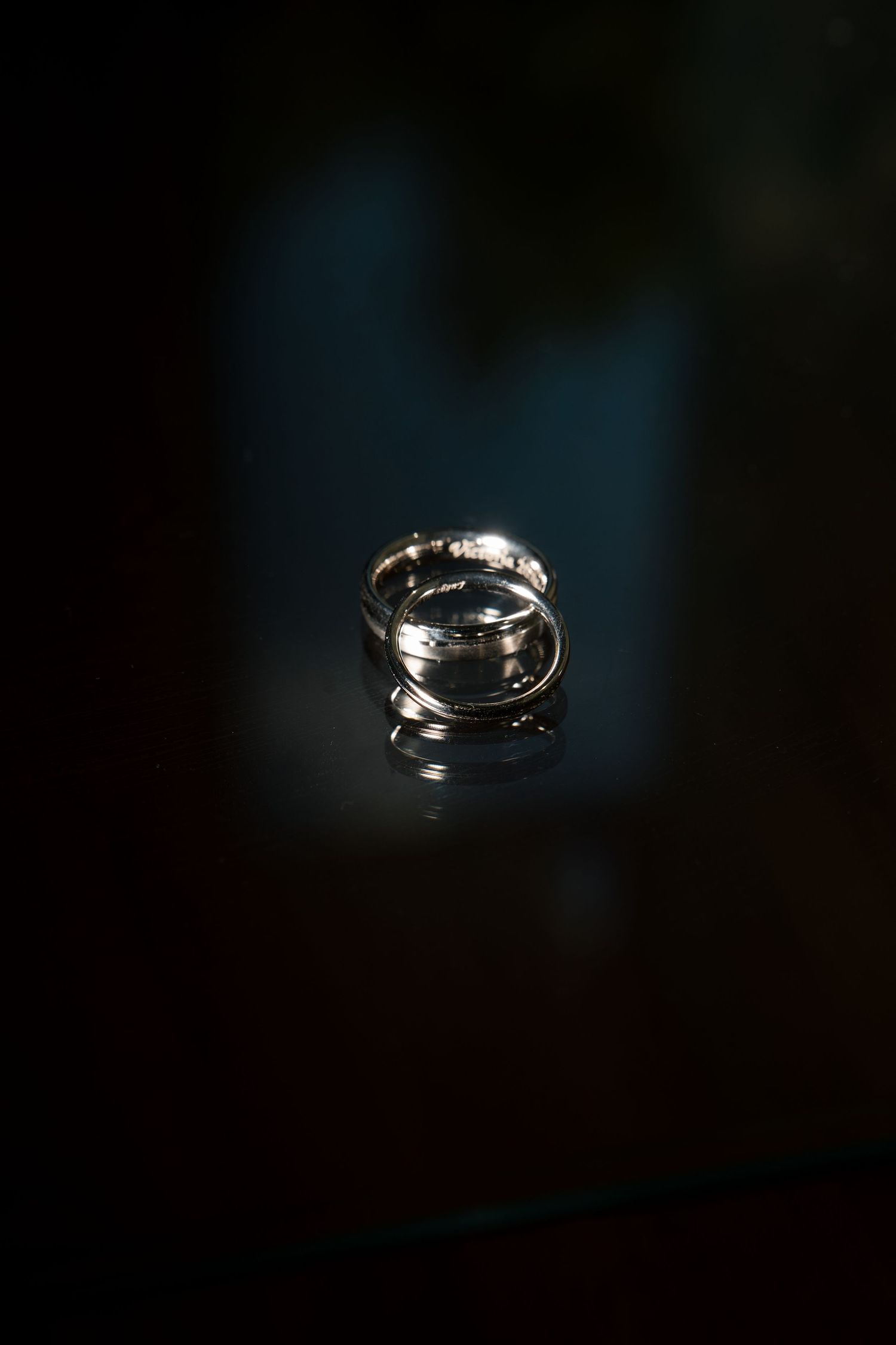 Two gold wedding rings stacked together on a dark reflective surface with dramatic lighting.