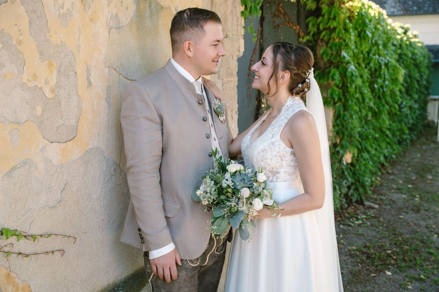 Elegant wedding portraits captured against a stone wall with climbing vines.