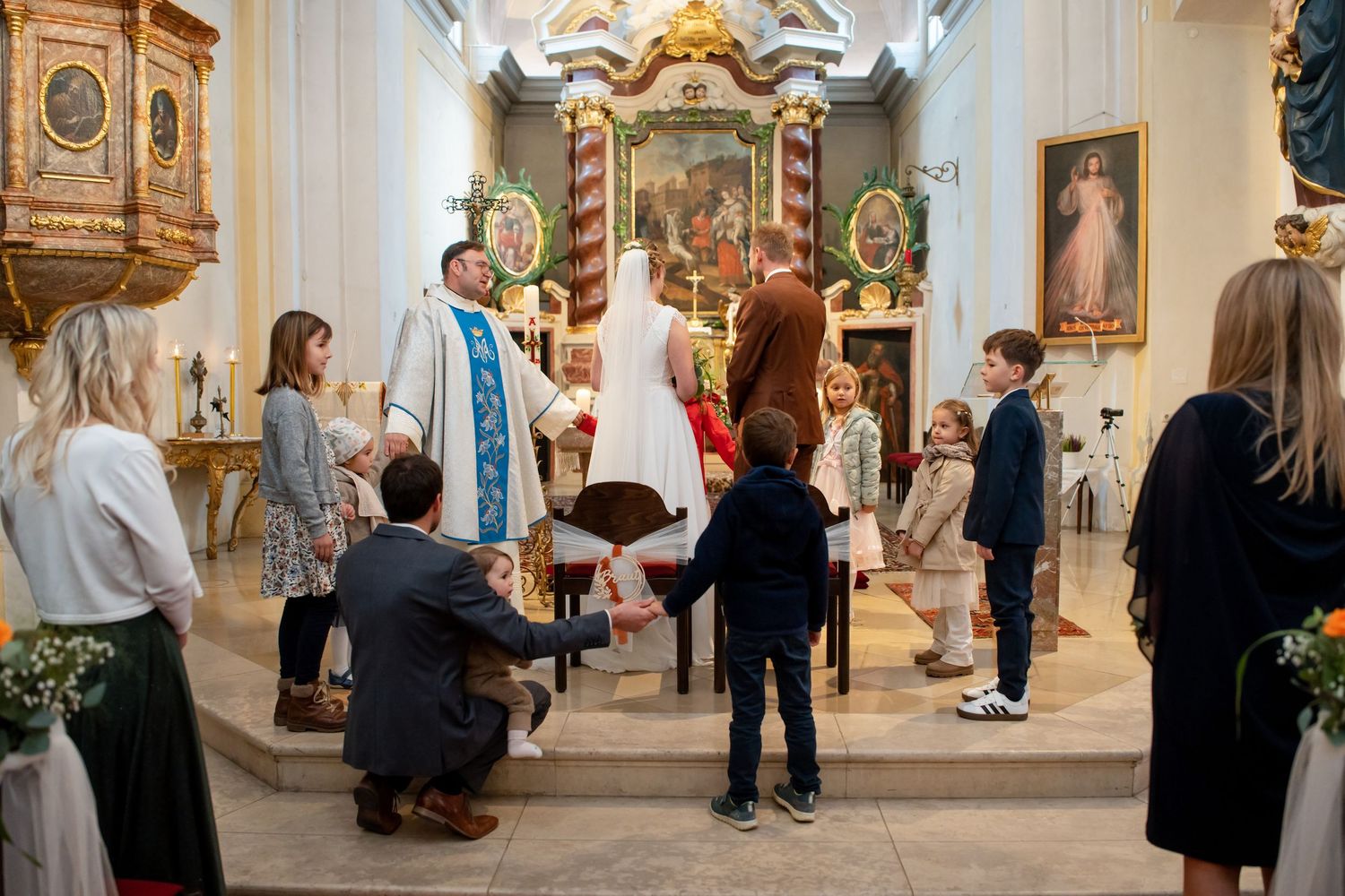 A priest performs a religious ceremony with attendees gathered in an ornate church interior.